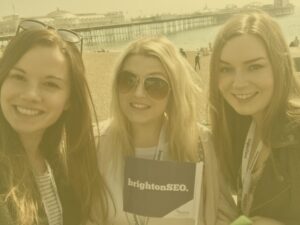 Hannah, Caroline, and Alex at Brighton beach on Brighton SEO day with yellow image overlay