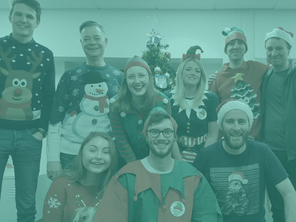 Team group shot in office wearing christmas outfits with teal overlay