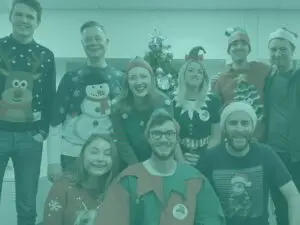 Team group shot in office wearing christmas outfits with teal overlay