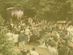 Blues and Rock in the Garden lots of people around a stage with yellow overlay