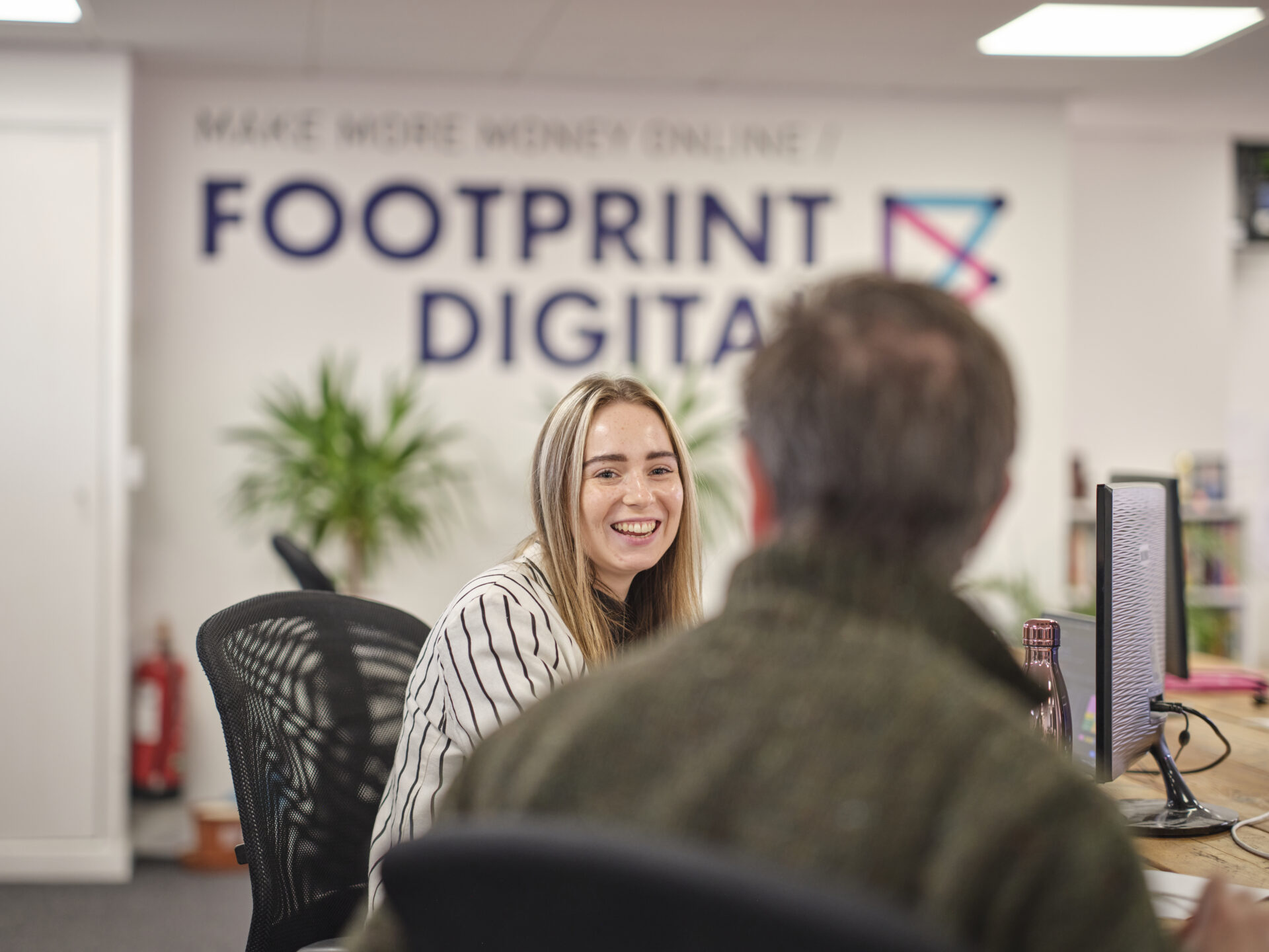 Full colour office shot with freya and mick having a discussion at their desks