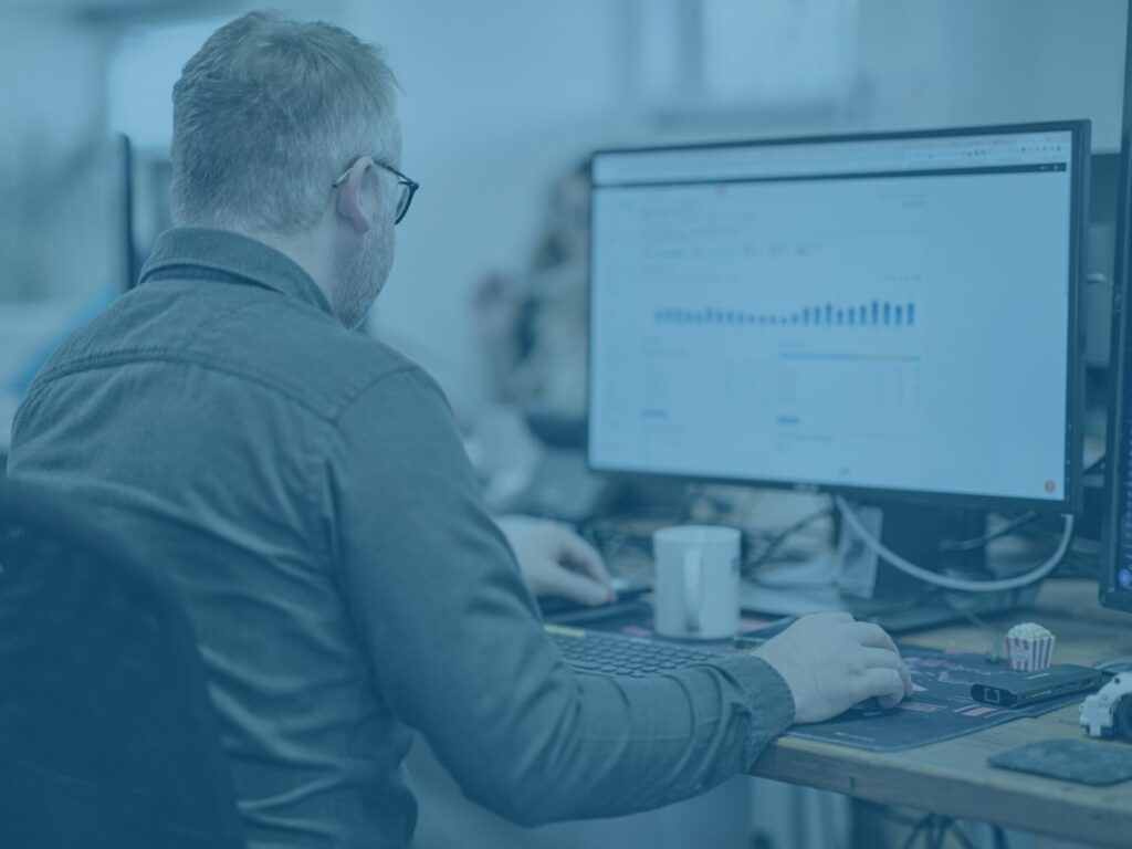 Blue office shot of sam looking at analytics on his desktop screen