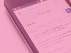 Pink close up of a mobile phone with 'analytics' being searched for on Google