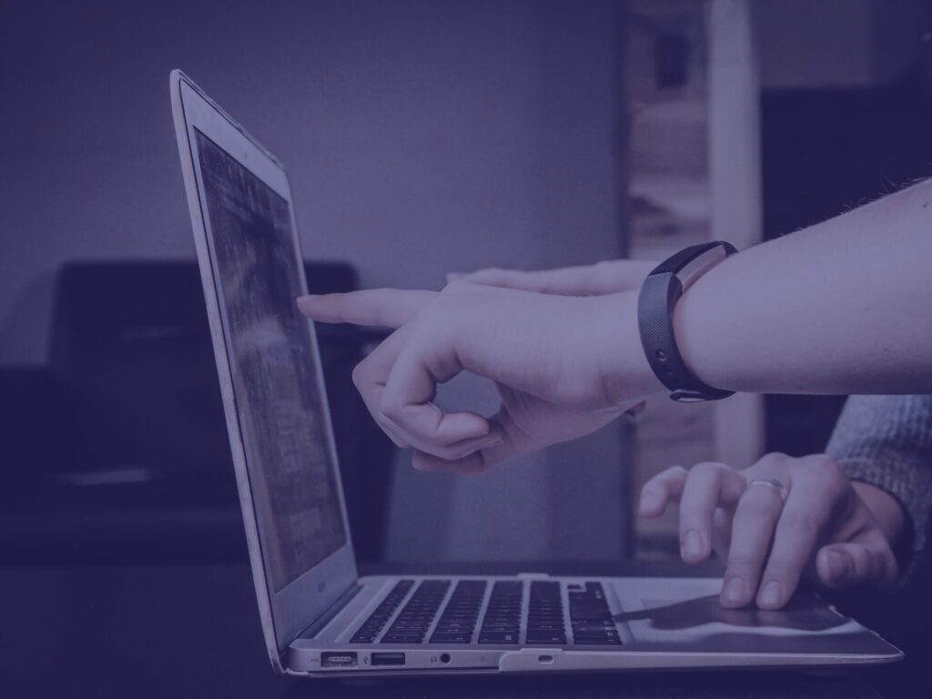 Navy open laptop on desk with someone pointing at the screen