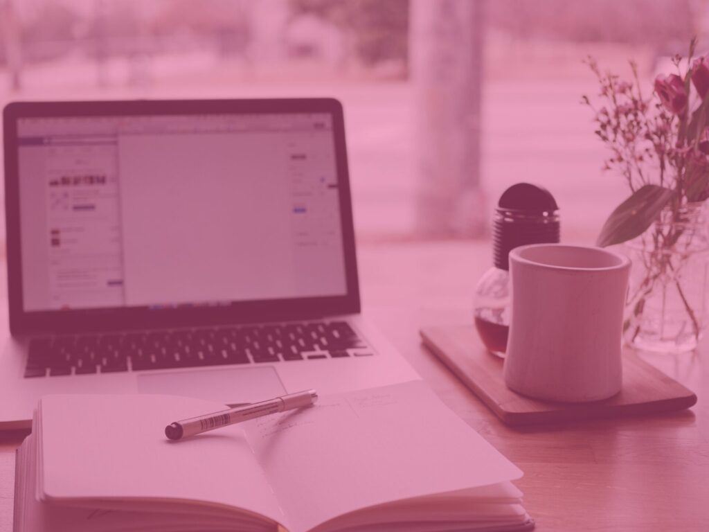 Pink open laptop and notepad with a coffee on a desk