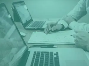 Teal close up of laptops and man writing on paper