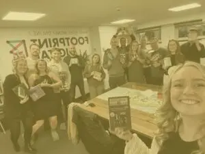 Thanksgiving 2024 group team selfie in the office with the team holding their winnings from the present game with yellow image overlay